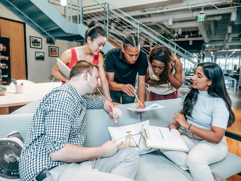 A diverse group of young adults collaborating on a project in a modern office setting.